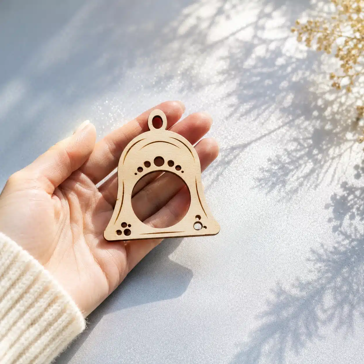 Serviettenring Weihnachtsglocke Jingle Bells aus Holz in Frauenhand auf blau-silbernem Hintergrund